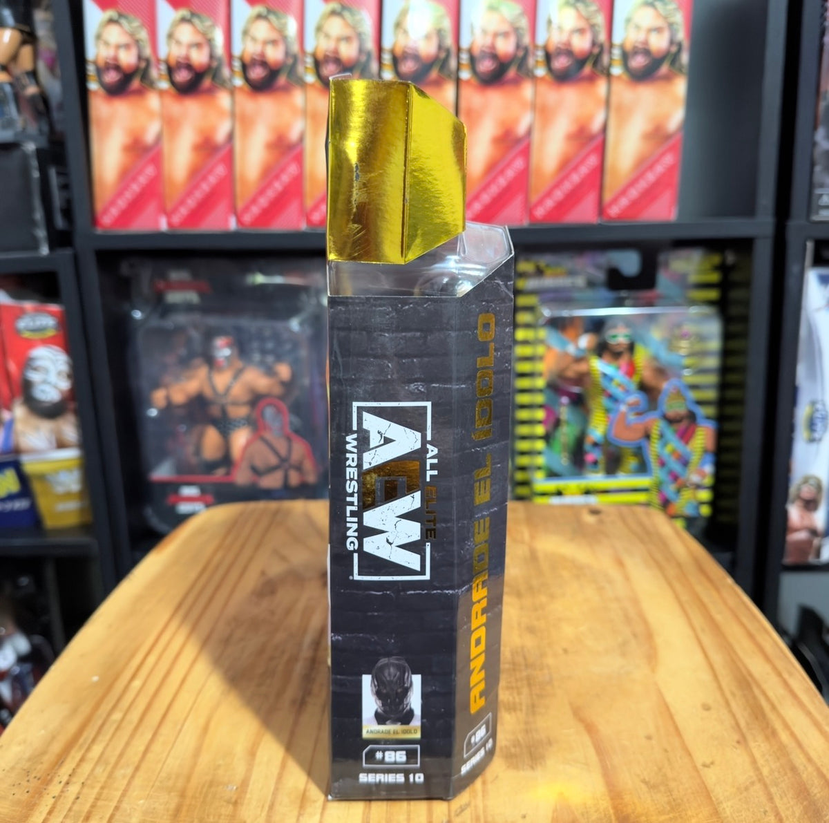 AEW wrestling figure box standing on table, gold top with black side panels