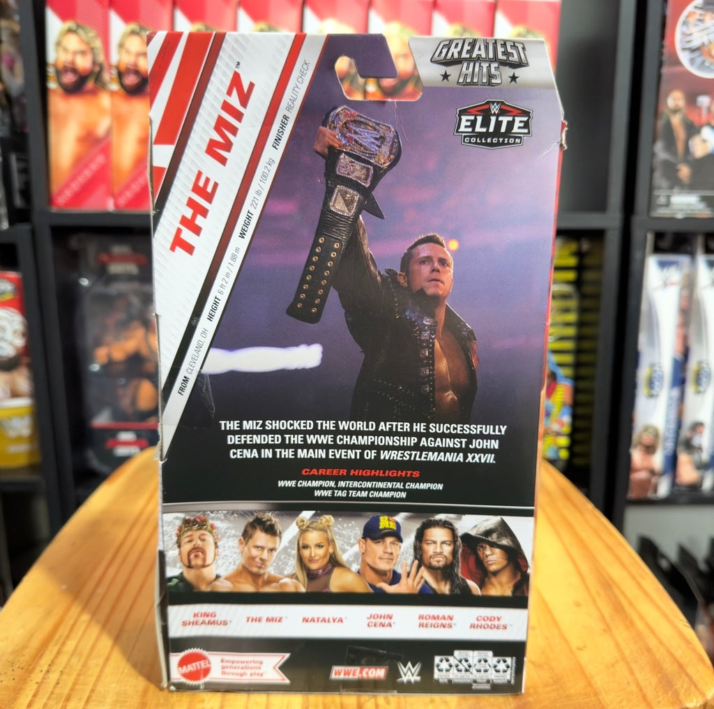 WWE Elite action figure box back panel with purple artwork and “Greatest Hits” badge.